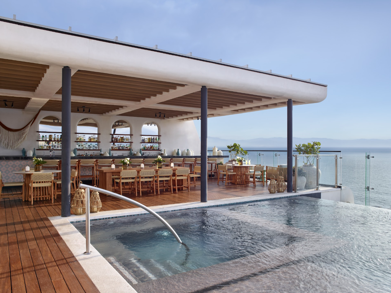 altorooftop1 be all inclusive Open-air seaside bar and restaurant on a wooden deck, with bottled drinks behind the bar and an ocean view behind.