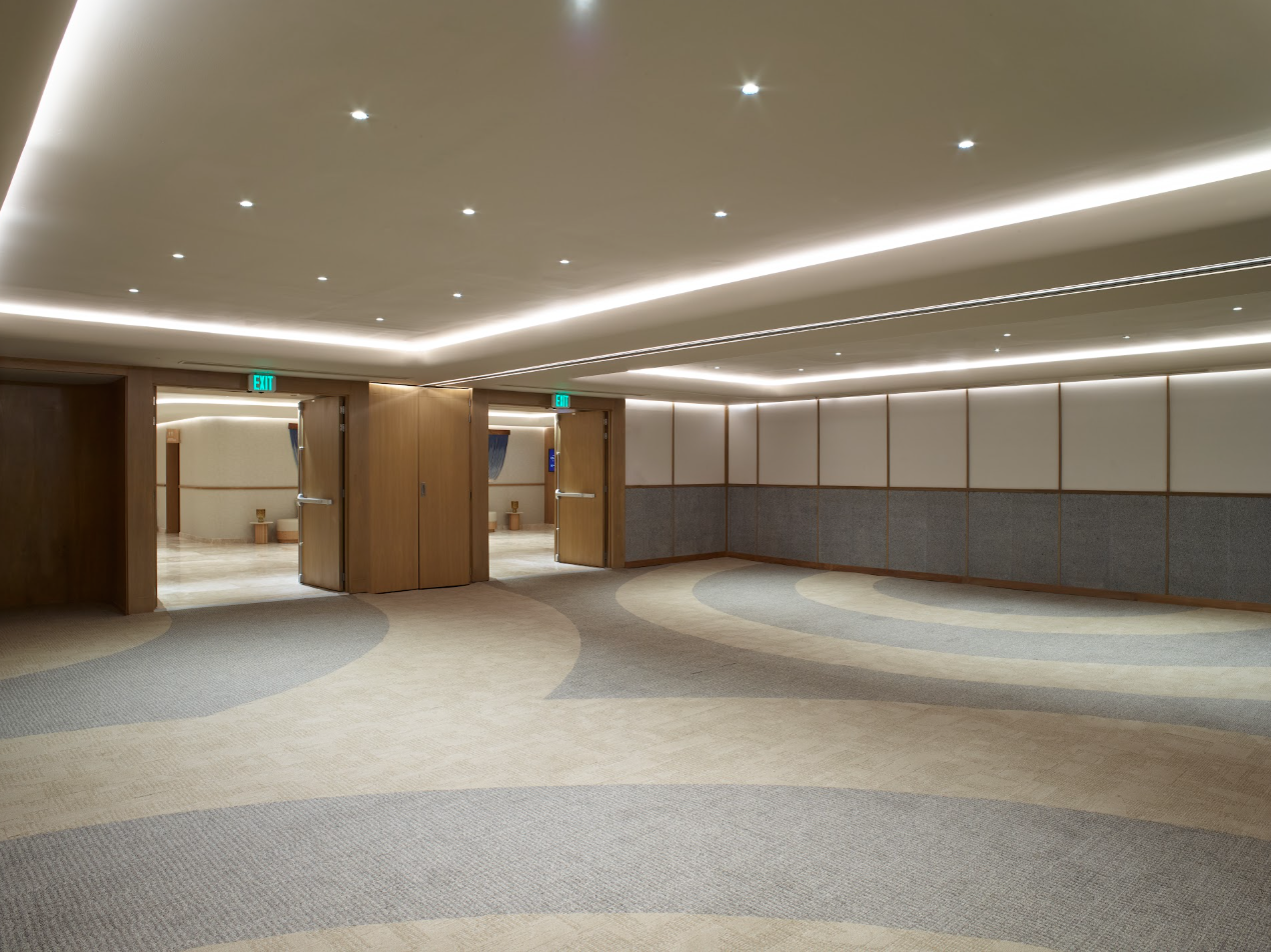 ballroom1 be all inclusive Bright, empty hotel lobby hallway with curved beige-gray carpet, wood panel walls, and double doors.