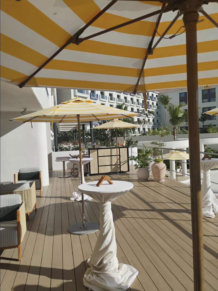 inezterr1 be all inclusive Outdoor hotel terrace with yellow-and-white striped umbrellas, high-top tables, and a bar in the background.