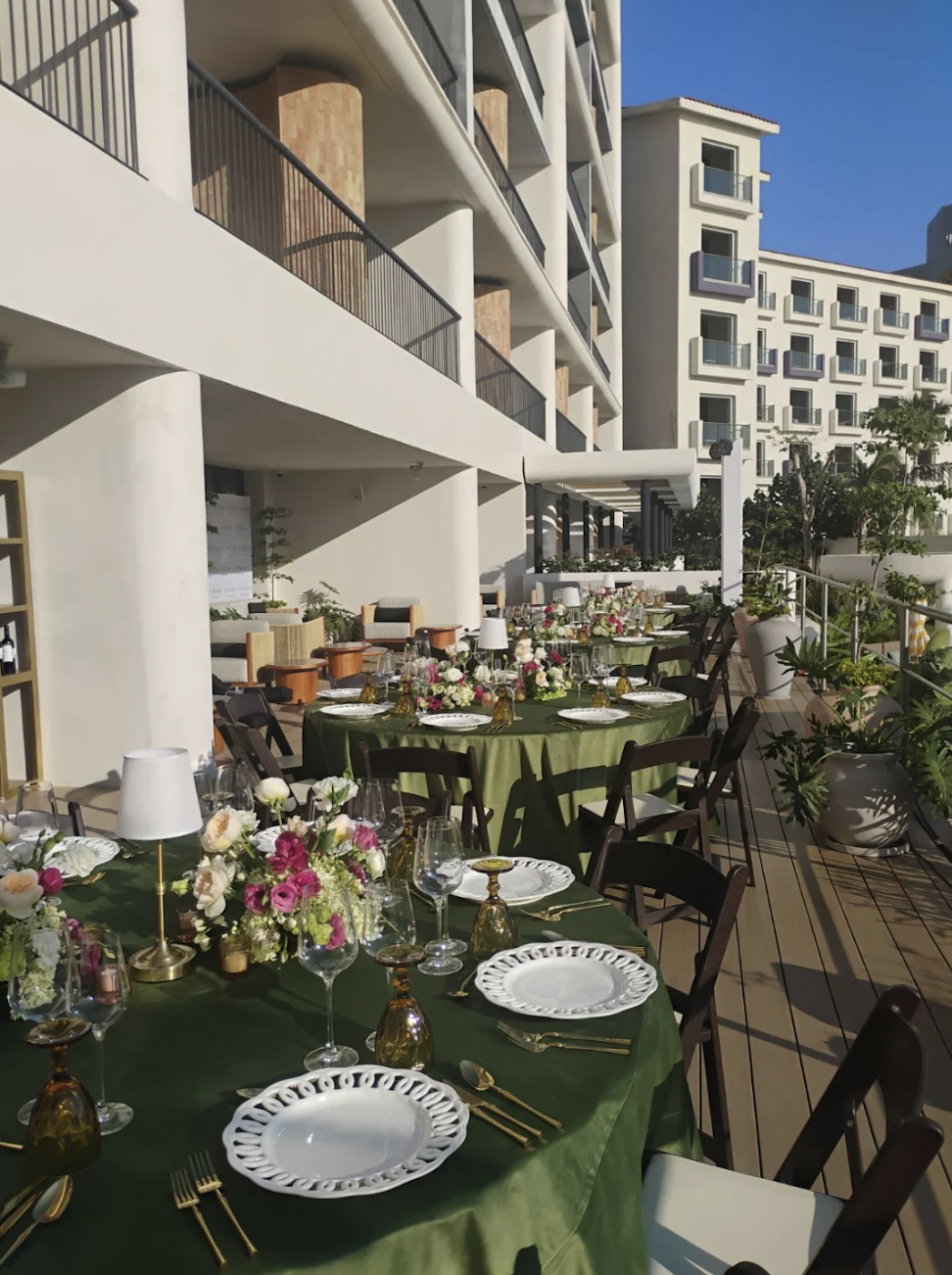 inezterr2 be all inclusive Outdoor hotel terrace set for a formal dinner with green tablecloths, floral centerpieces, and gold-flatware against modern white buildings and blue sky.