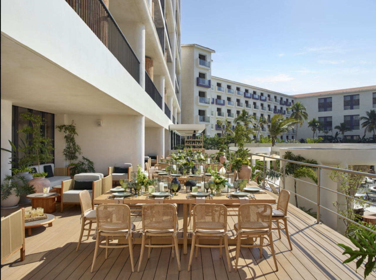 inezterr4 be all inclusive Sunlit hotel terrace with a long dining table set for a meal, beige wicker chairs, and potted plants.