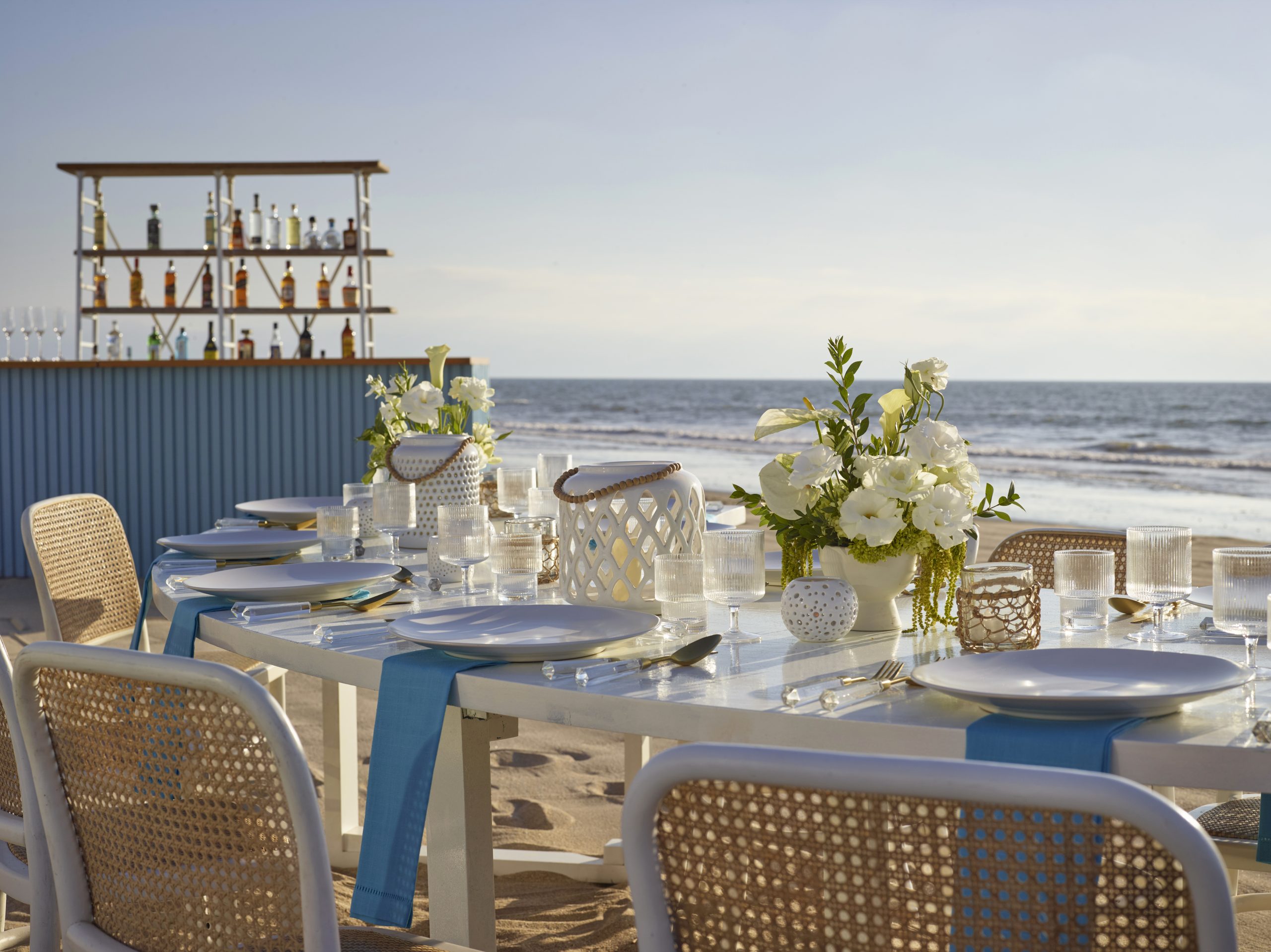 beach vendor set up detail be all inclusive Outdoor beachside dining setup with white tables, blue napkins, glassware, and floral centerpieces facing the ocean.