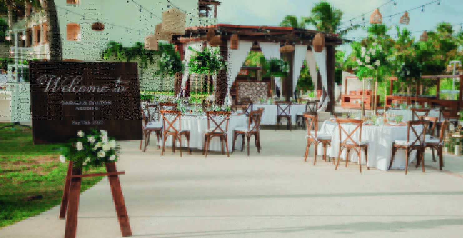 5 be all inclusive Outdoor wedding reception with round tables, white linens, and wooden chairs; a welcome sign on an easel reads 'Welcome to Sarah & Dalton Wedding May 13th, 2023'.