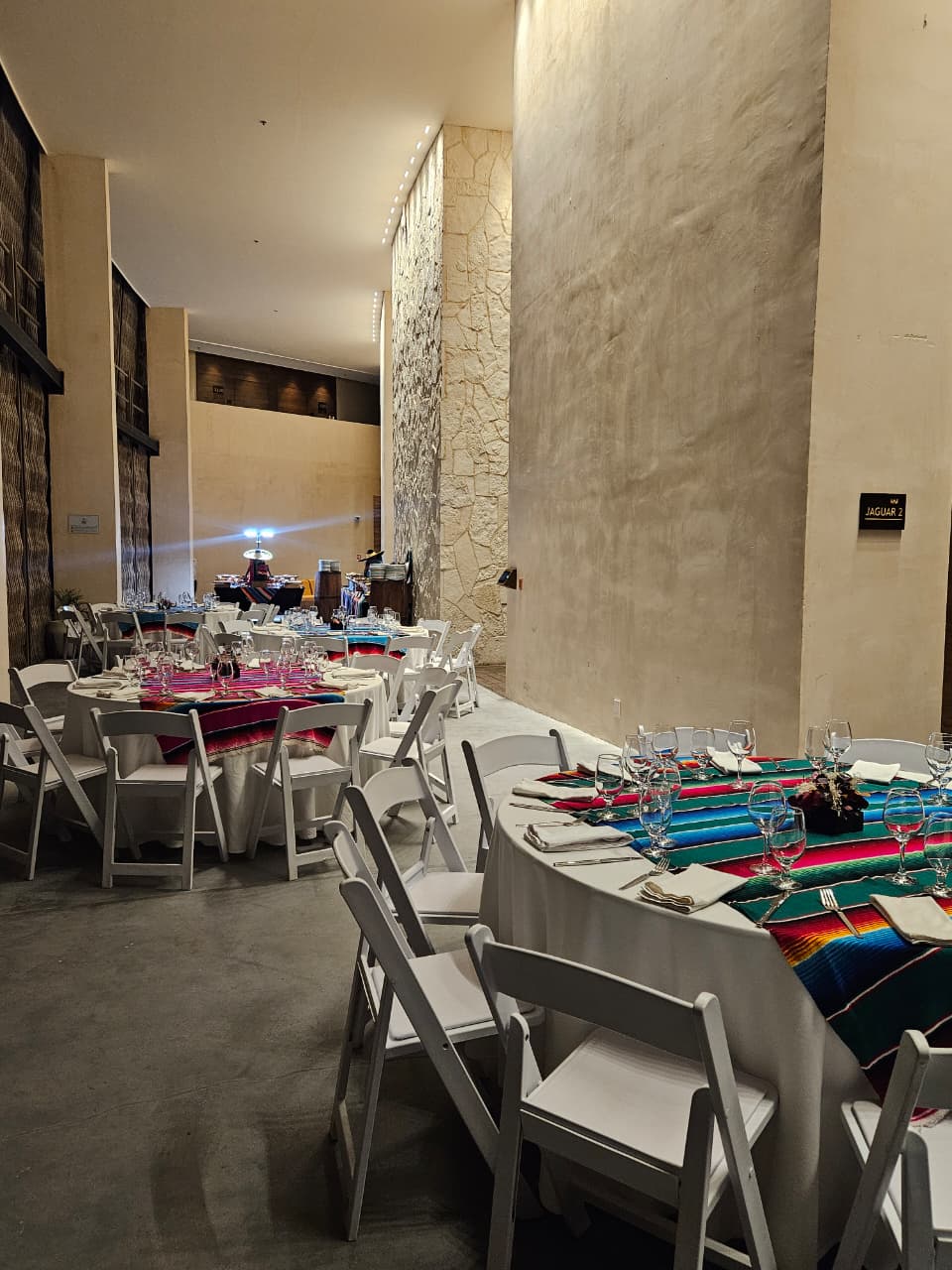 foyer 4 be all inclusive Banquet hall set for a formal dinner with round tables, white chairs, white tablecloths, and colorful striped runners with glassware.