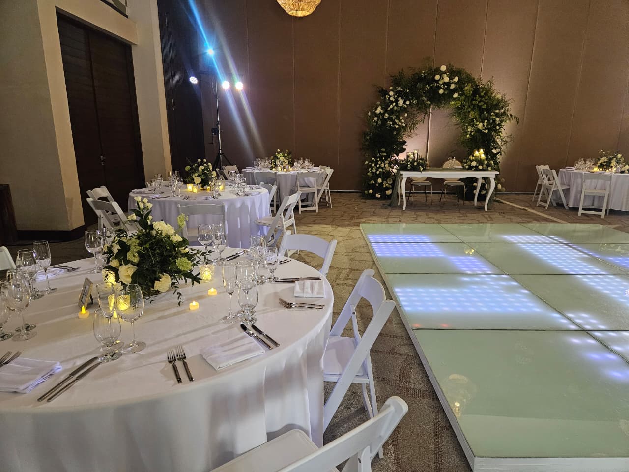 jaguar b 20 1 be all inclusive Elegant banquet hall setup with round white-draped tables, floral centerpieces, and candlelit ambiance; a illuminated glass dance floor on the right remains.