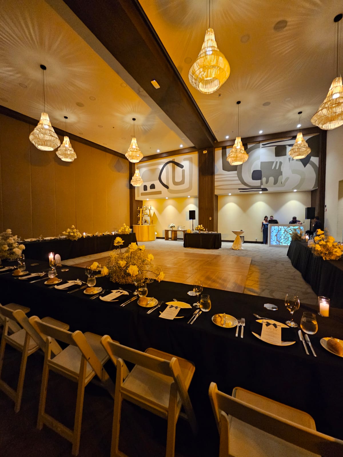 jaguar b 5 be all inclusive Banquet hall with long black-table setup, yellow floral centerpieces, candles, and warm pendant lights over a wooden dance floor.