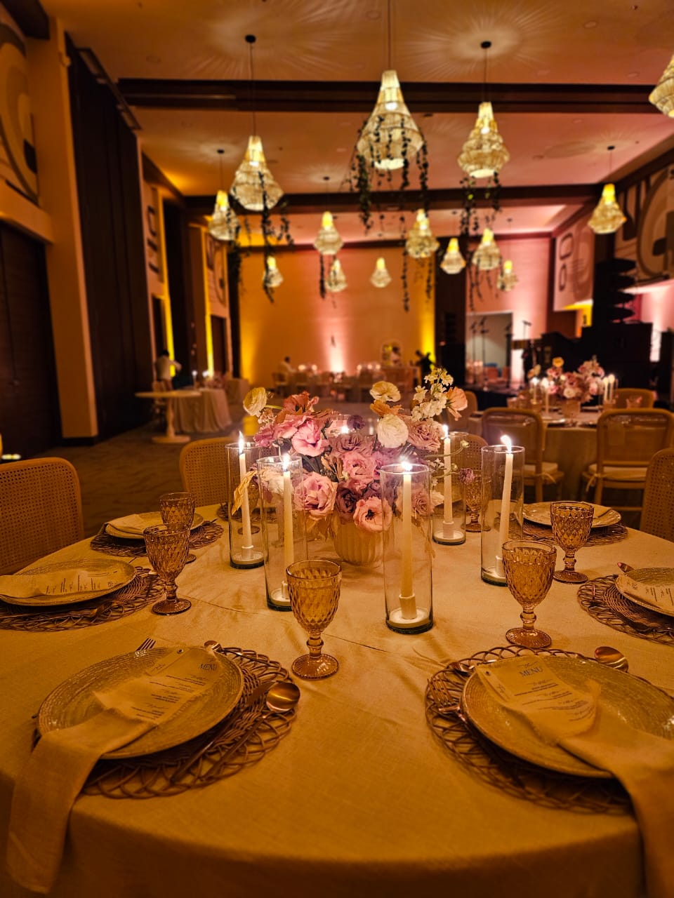 jaguar b 9 be all inclusive Round table set for a formal event with a pink floral centerpiece, candles, and gold-rimmed glassware in a warmly lit ballroom.