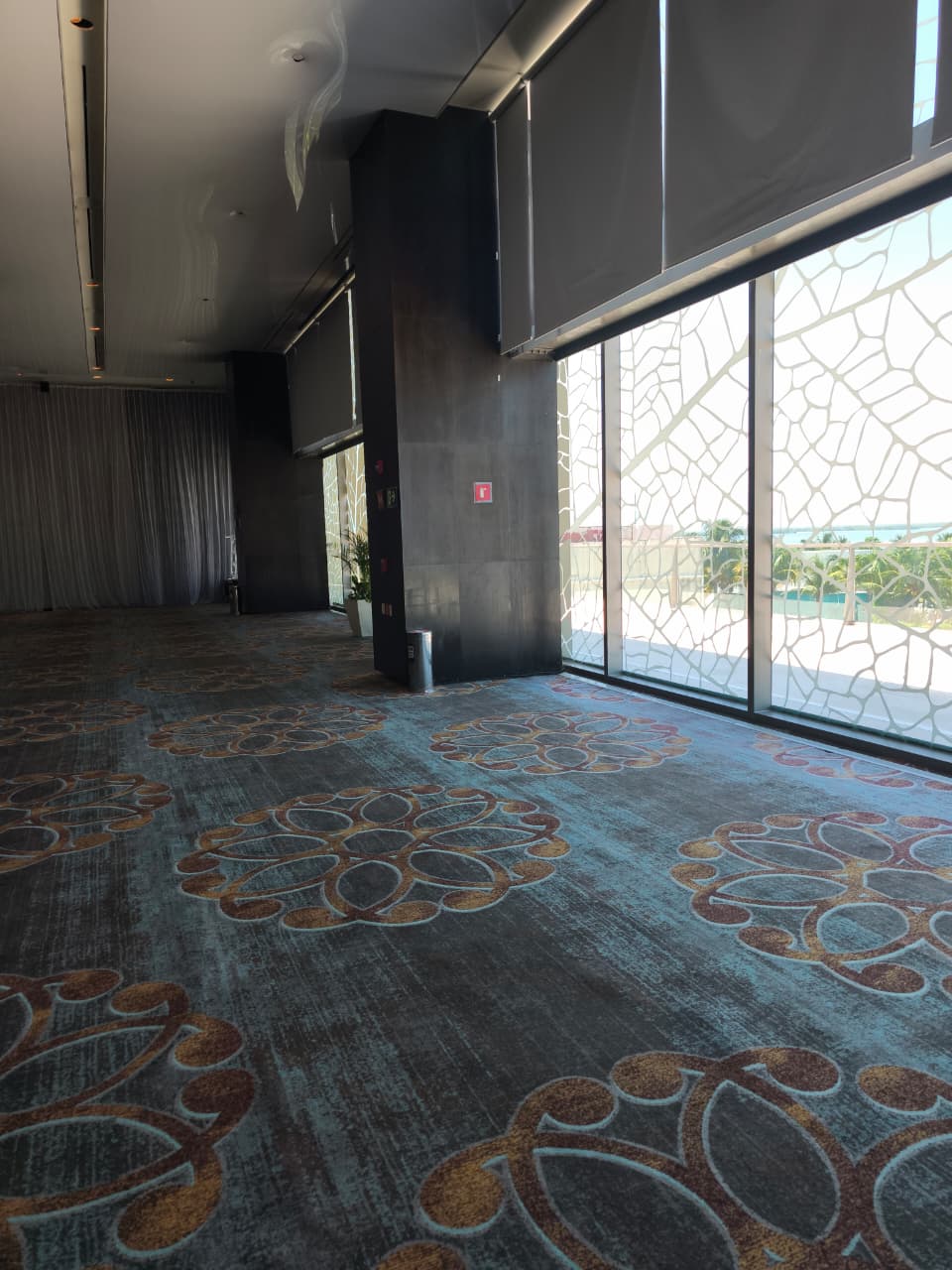 salon ch 1 be all inclusive Open hotel lobby or hallway with patterned carpet, dark walls, and large windows along the right; natural light streaming in.
