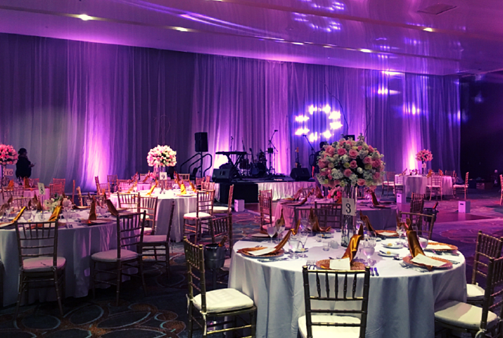 screenshot 20260609 120356 be all inclusive Elegant banquet setup with round tables, pink floral centerpieces, and purple stage lighting in a ballroom venue to host a formal event.
