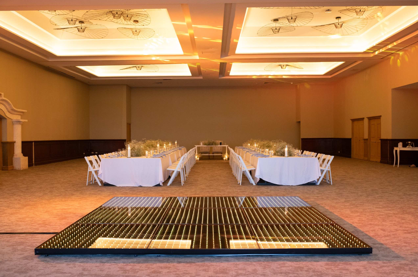 screenshot 20260616 143100 be all inclusive Banquet hall with two long white-draped dining tables set for a formal dinner, candles and greenery centerpiece, and an illuminated glass dance floor in the foreground.