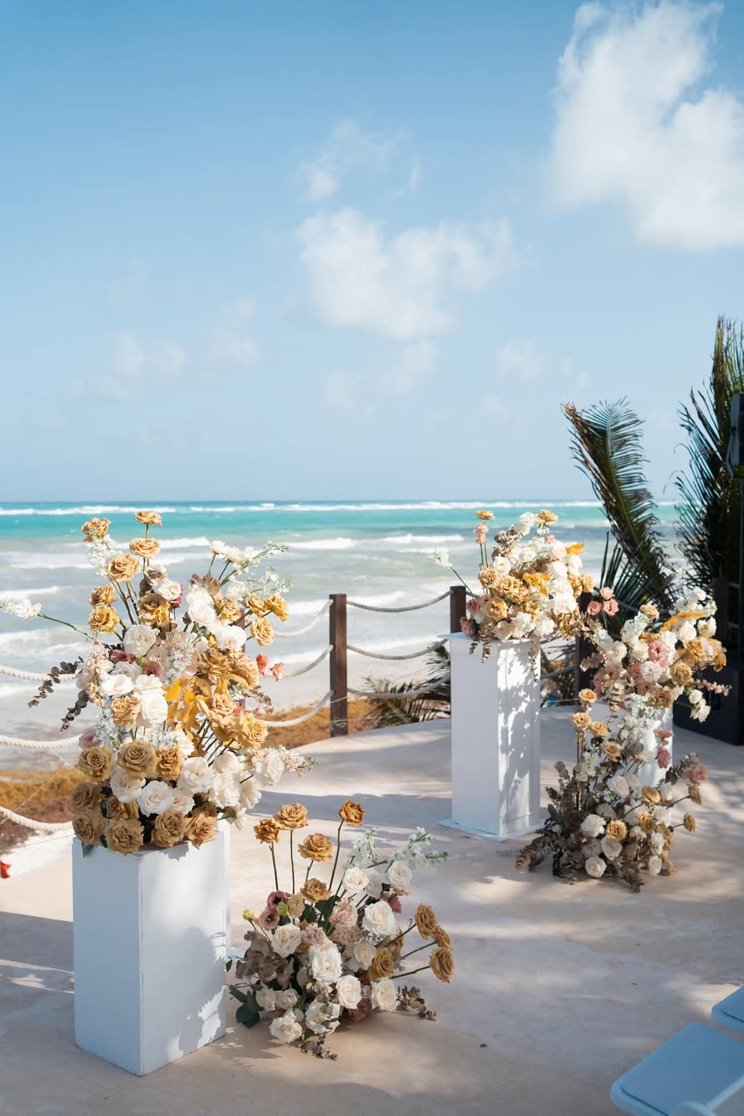 willys 1 be all inclusive Beach wedding ceremony setup with cream and blush florals on white pedestals along a sandy path by the ocean.