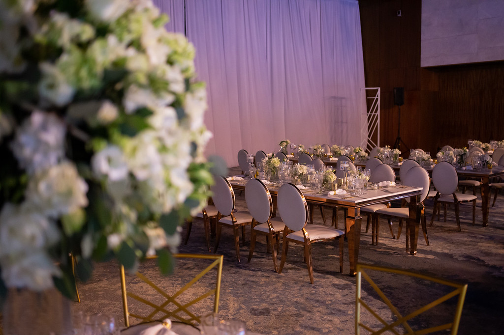 isp4mrknxljpg be all inclusive Elegant banquet tables set for a formal event with white floral centerpieces and white cushioned chairs visible in a softly lit venue.