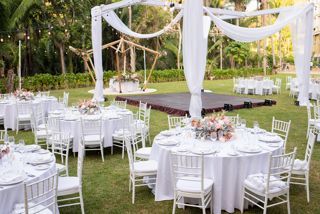 ihv6df4nxljpg683f5afb1820c be all inclusive Outdoor wedding reception setup with round tables, white chairs, and floral centerpieces on a grassy lawn under draped white fabric.