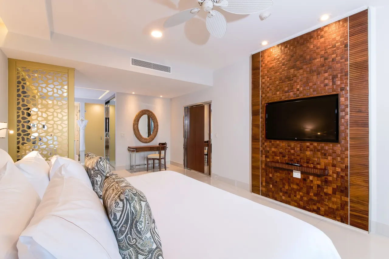 0225a12000k7e3wm70d76w1280853r5 be all inclusive Hotel room with a large bed, patterned pillows, and a wooden mosaic TV wall across from the bed.