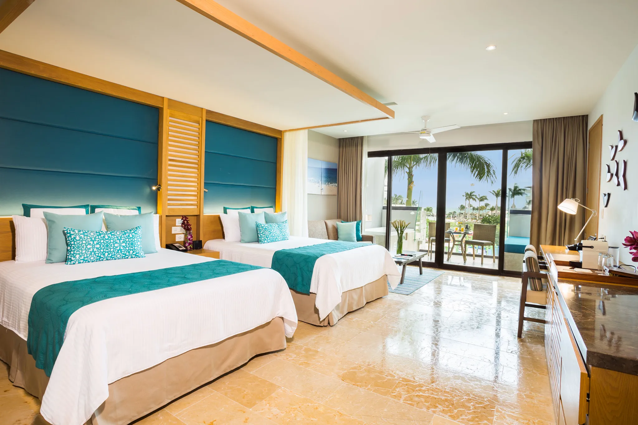 drepmjrgvdblap be all inclusive Hotel room with four beds, teal cushions, and wood accents, opening to a balcony with palm trees outside.