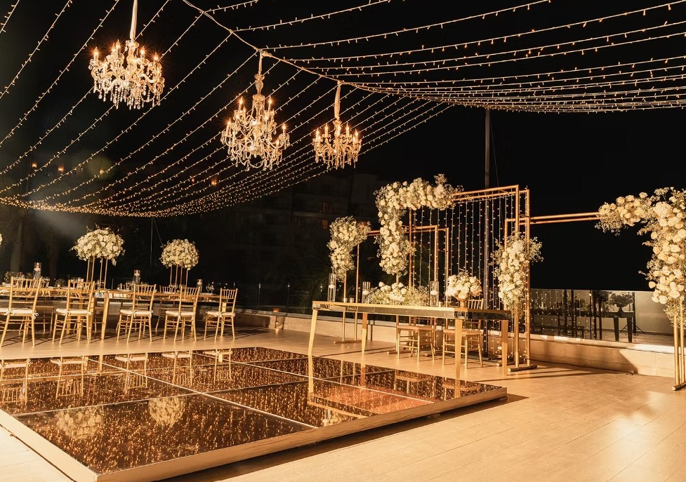 screenshot 20260713 165445 be all inclusive Elegant outdoor wedding reception at night with gold decor, chandeliers, string lights, and a mirrored dance floor.