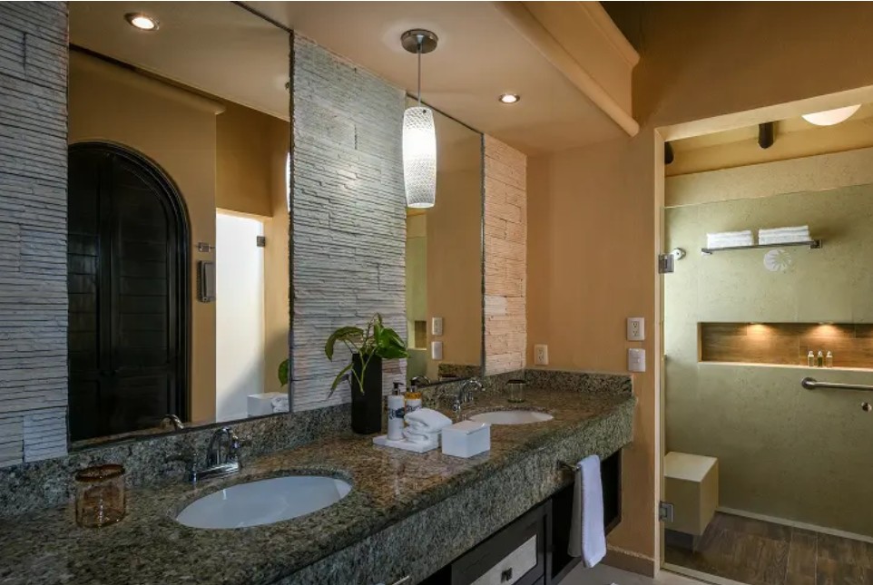 screenshot 20260722 140336 be all inclusive Hotel bathroom vanity with granite counter and double sinks, mirrors, and a potted plant above the sink.