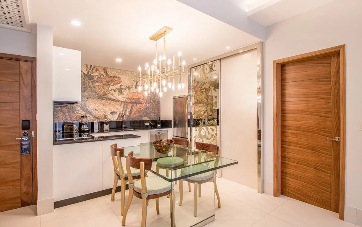 screenshot 20260728 093205 be all inclusive Modern kitchen with glass dining table and six wooden chairs, mosaic backsplash, and a chandelier.