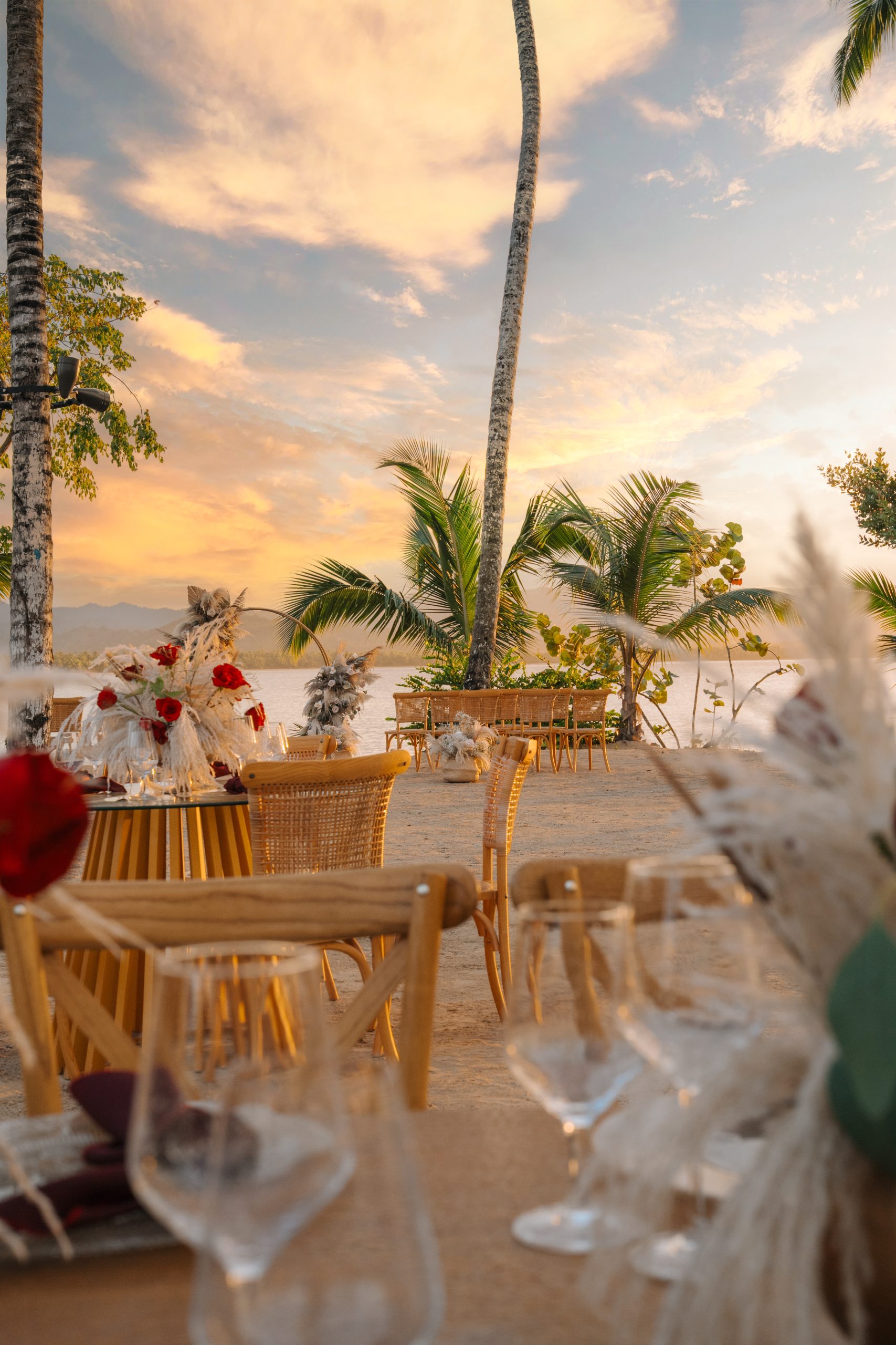 zemimichesbeacheventdinner 3 be all inclusive Beachside outdoor dining setup with wooden chairs, glassware, and floral decorations at sunset by the water
