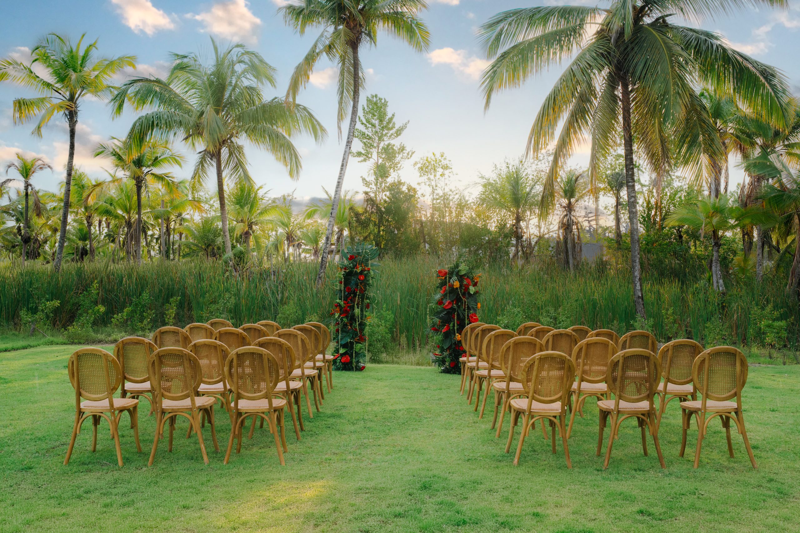 zemimichesgardenweddingceremony 6 be all inclusive Outdoor wedding ceremony setup with rows of brown chairs on a green lawn under palm trees and tropical plants