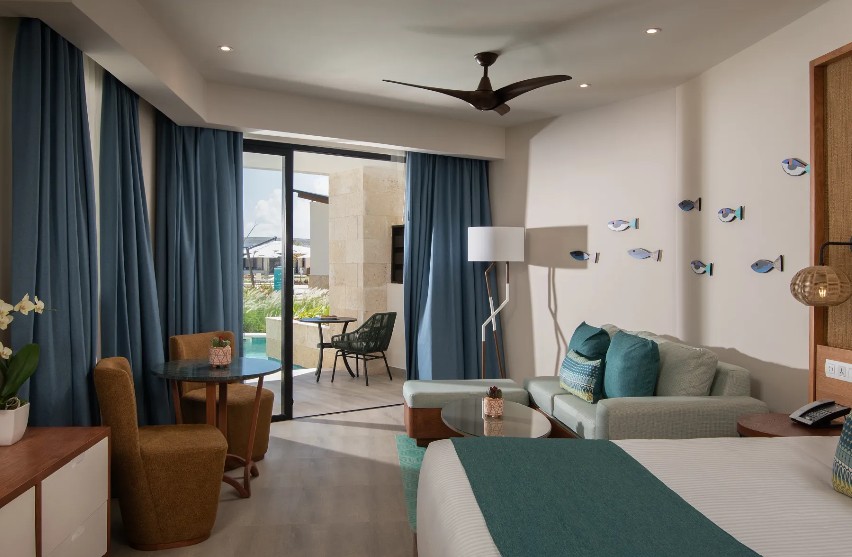 screenshot 20260805 093818 be all inclusive Hotel room with a king bed, teal accents, and a seating area leading to a balcony.