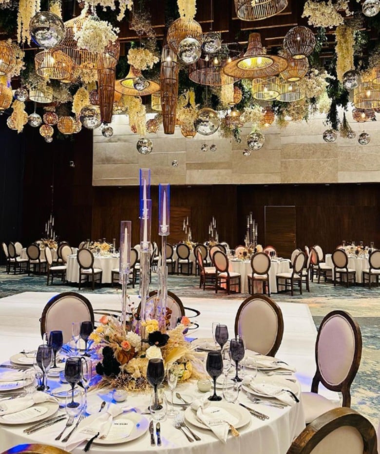 screenshot 20260819 093916 be all inclusive Elegant banquet hall with ornate hanging lights, round tables set for a formal dinner with floral centerpieces.
