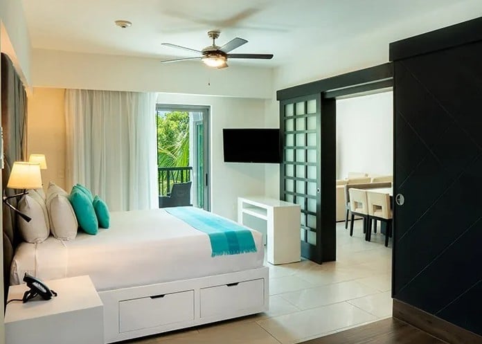screenshot 20260928 102033 be all inclusive Hotel room with a large white bed, turquoise accents, and a balcony view through sliding doors