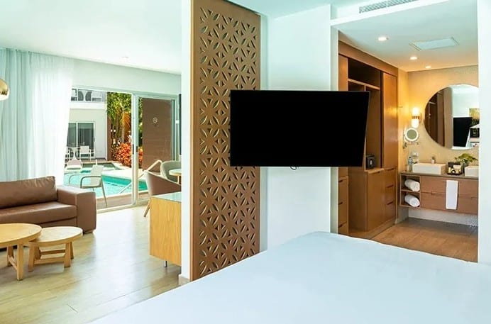 screenshot 20260928 102235 be all inclusive Hotel suite with a seating area, glass doors to a pool courtyard, and a wall-mounted flat-screen TV on a decorative screen.
